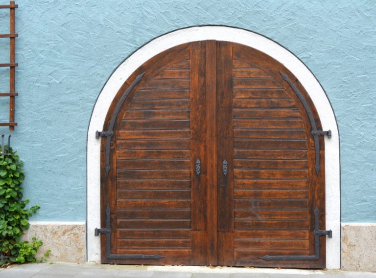Grande porte en bois cintrée sur une façade bleue
